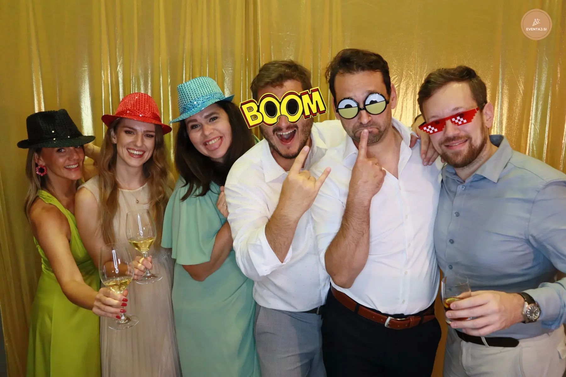 Skupina gostov s Photo Booth rekviziti pred zlatim ozadjem
